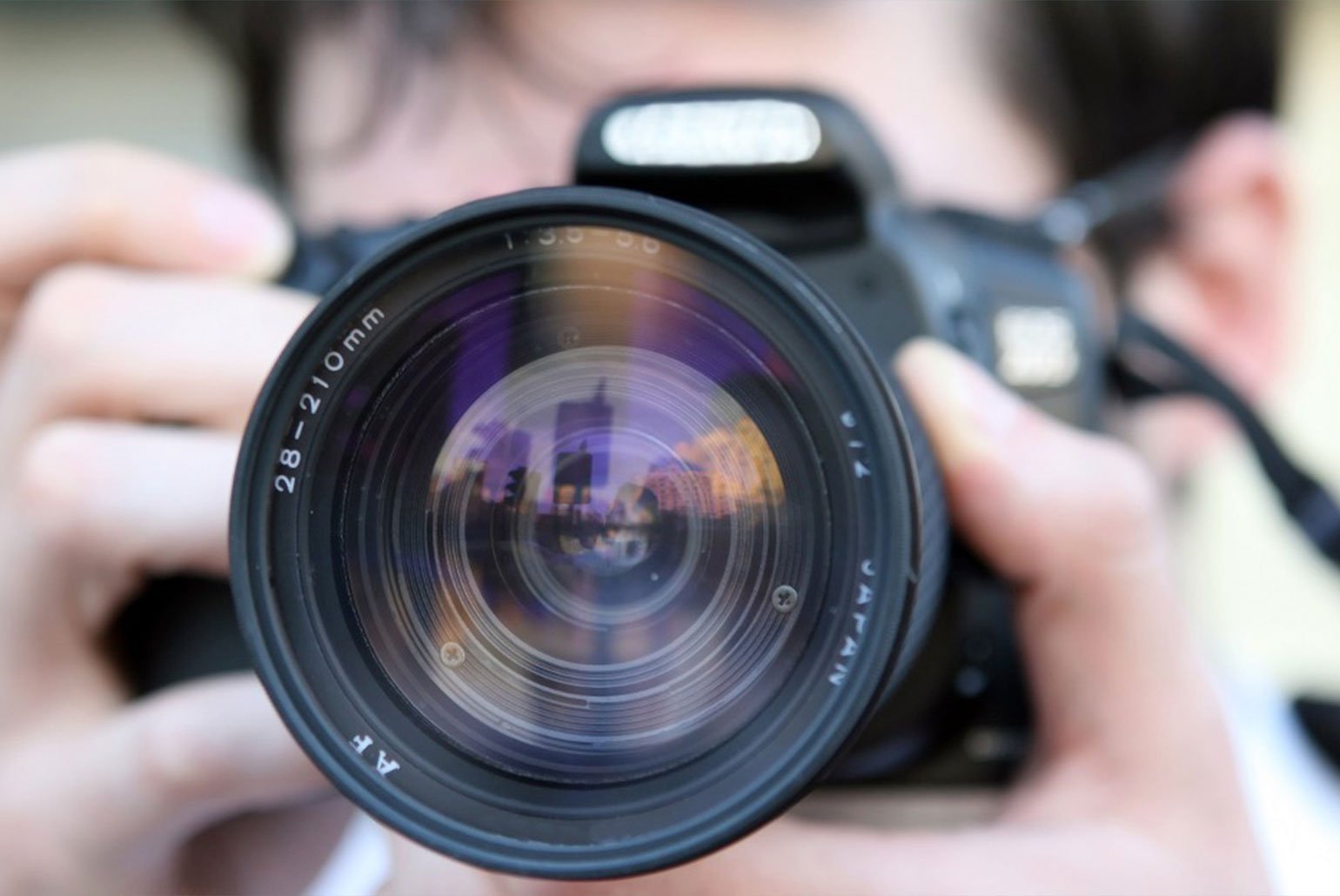 Gros plan sur l'objectif d'un appareil photo reflétant un paysage urbain avec des grattes-ciel.