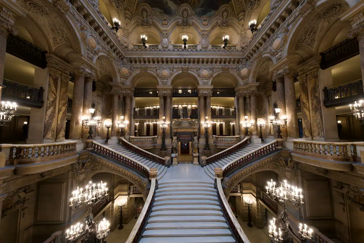 Grand escalier majestueux décoré de colonnes et lustres dans un opéra historique.
