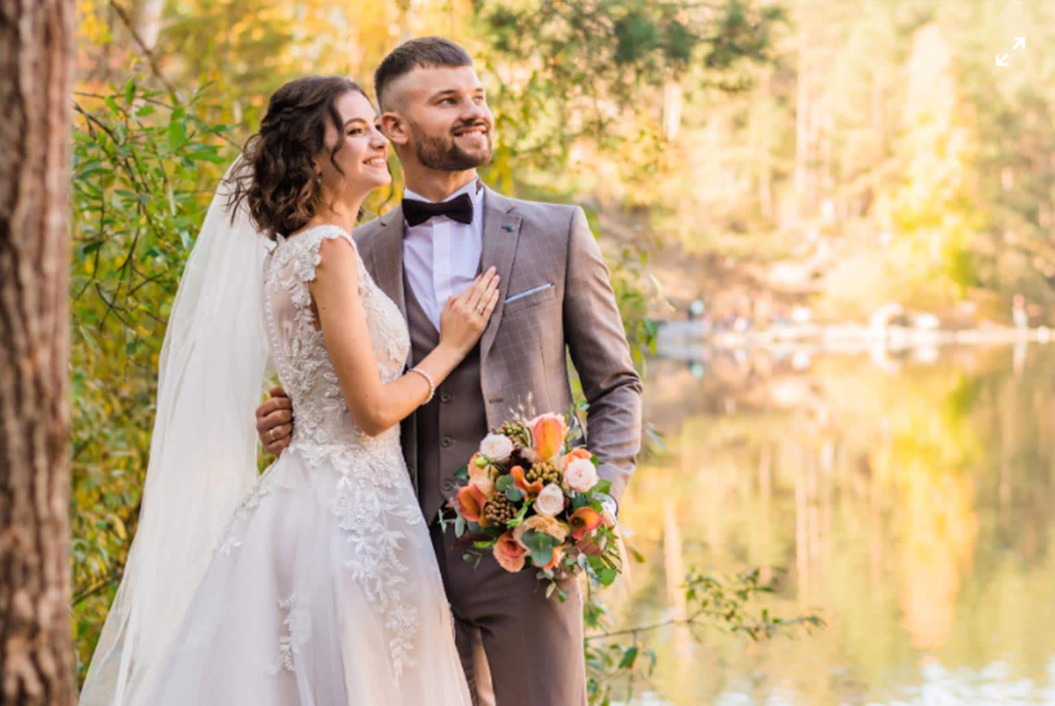 Un couple de mariés posant dans un cadre naturel avec des arbres et un lac en arrière-plan