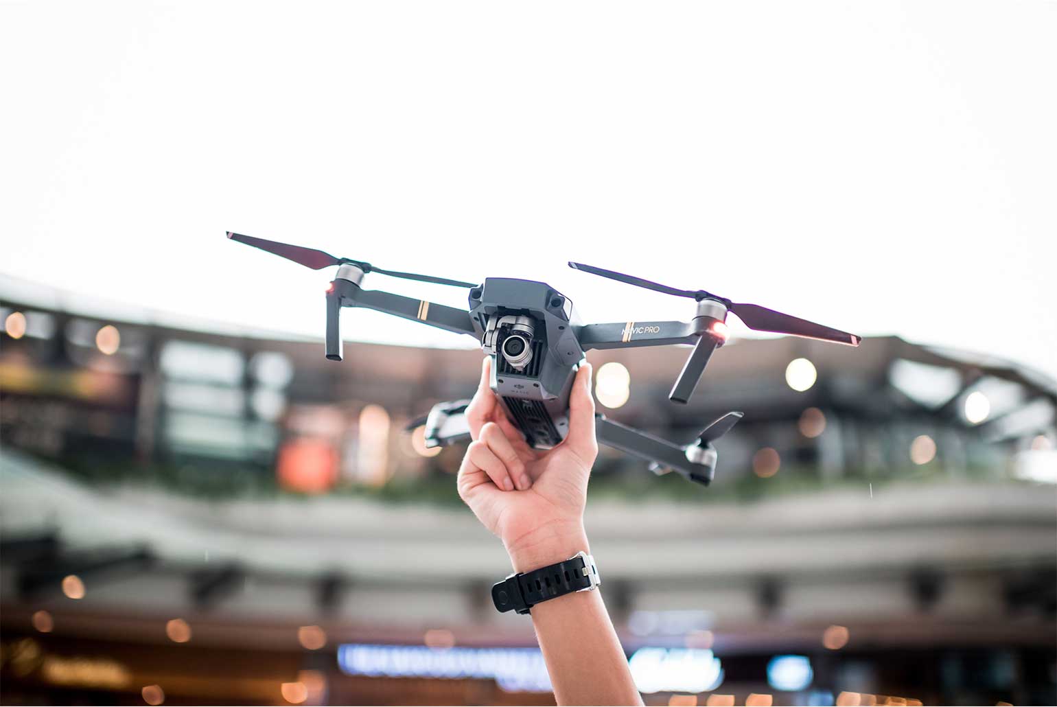 Une main tient un drone en vol stationnaire dans un environnement urbain.