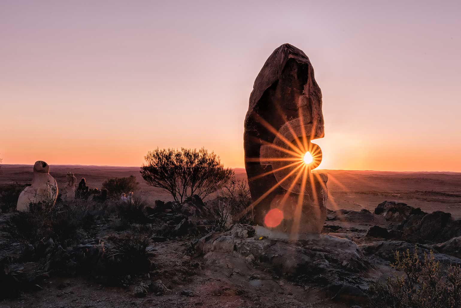 Lever de soleil à travers une sculpture en pierre dans un paysage désertique.