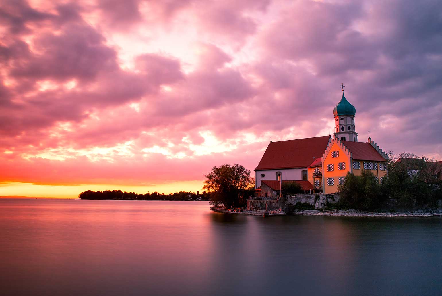 Église pittoresque au bord d'un lac sous un ciel coloré au coucher du soleil