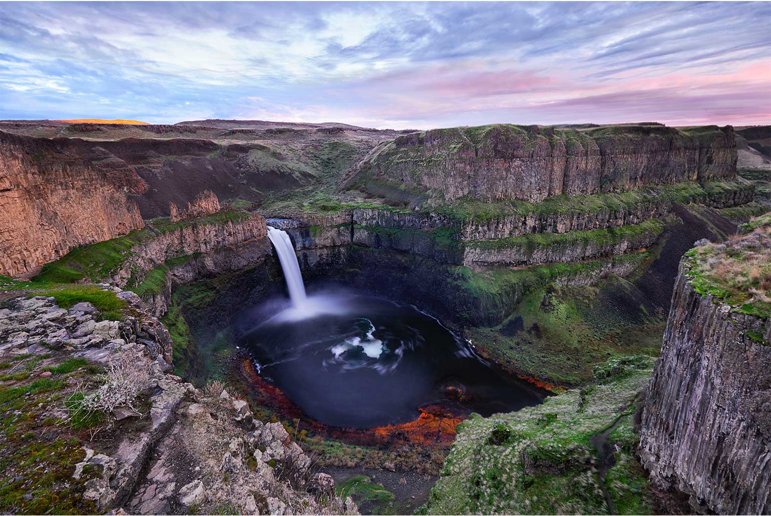 Cascade majestueuse entourée de falaises verdoyantes dans un paysage naturel au coucher du soleil