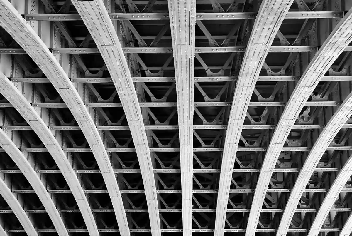 Structure métallique arquée sous un pont en noir et blanc