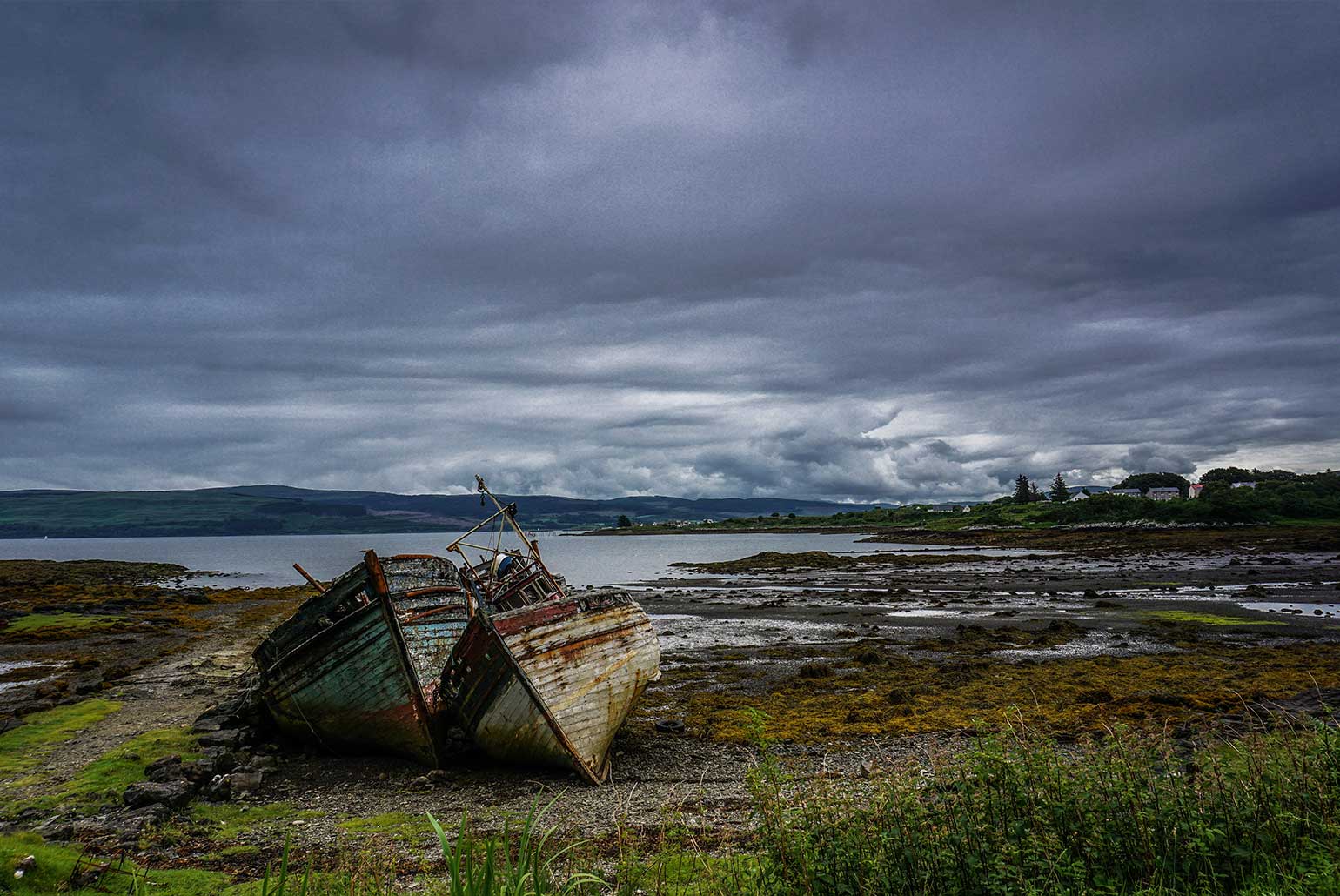 Deux bateaux en bois abandonnés sur une côte rocheuse sous un ciel nuageux.