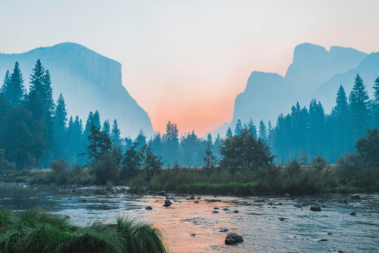 Paysage de montagne avec une rivière au premier plan et un ciel coloré au coucher du soleil.
