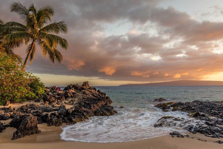 Plage tropicale avec palmiers et formations rocheuses au coucher du soleil.