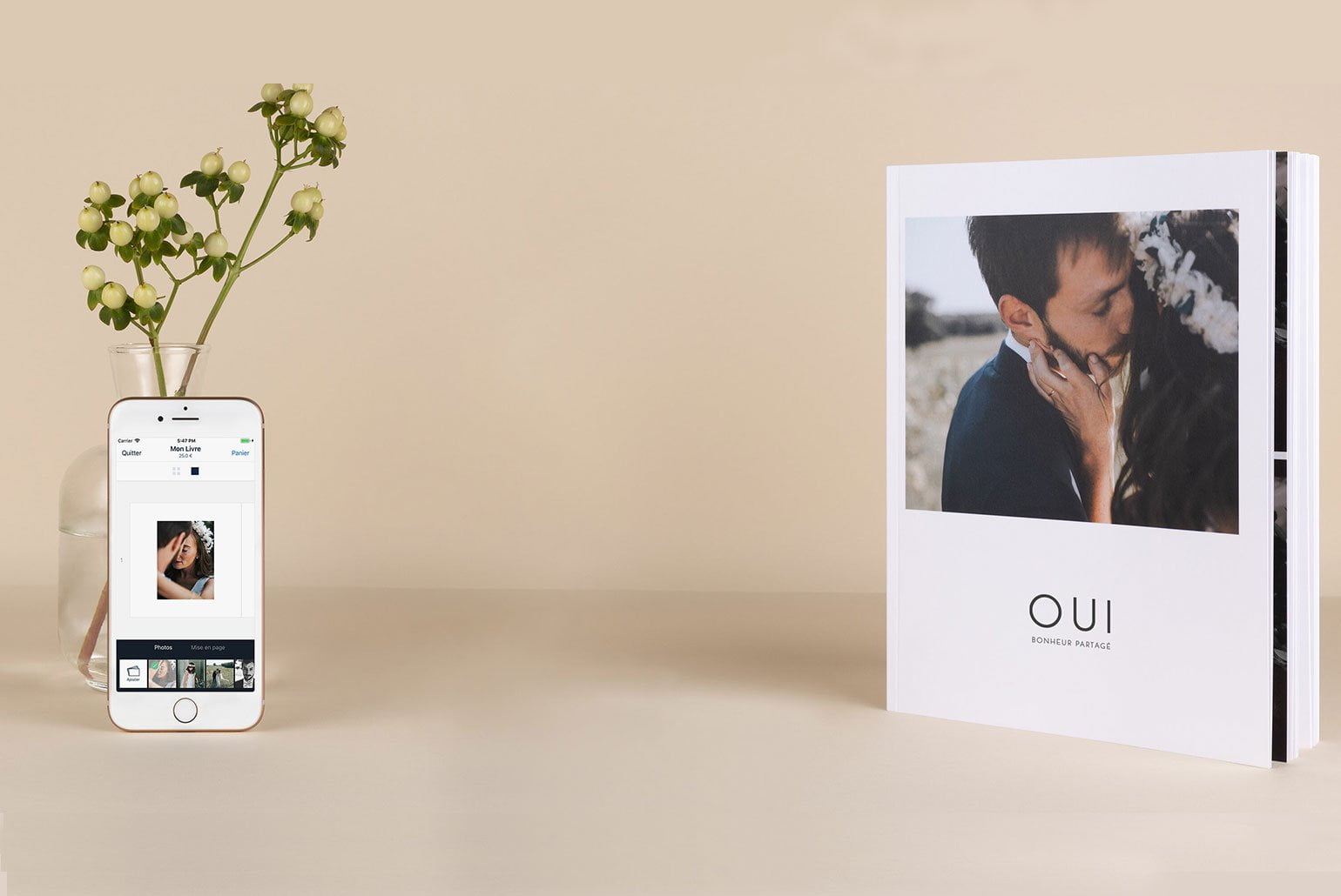 Photobook de mariage avec un vase et un smartphone affichant une photo sur une table beige.
