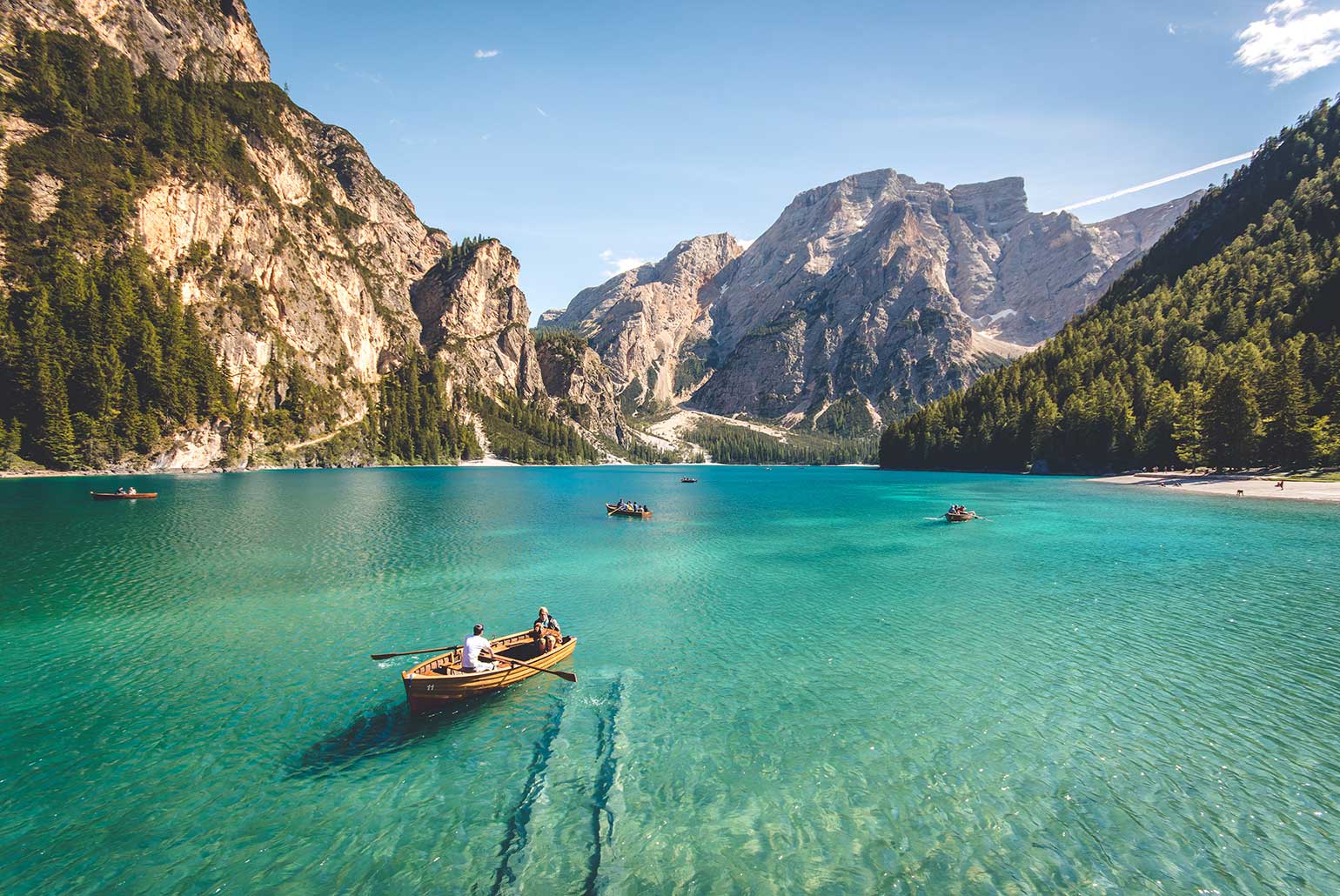 Un lac turquoise entouré de montagnes avec des barques à la surface de l'eau.