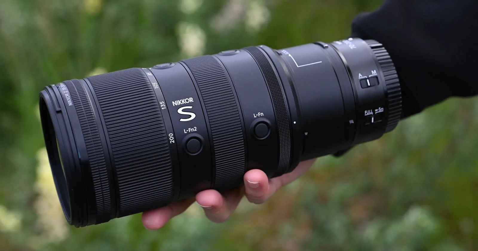 Nikon Nikkor Z 70-200 mm f/2.8 VR S II tenu en main, fond végétal flou en extérieur