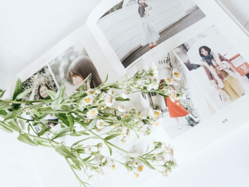 Livre ouvert avec photos de mode, décoré de fleurs blanches et jaunes.