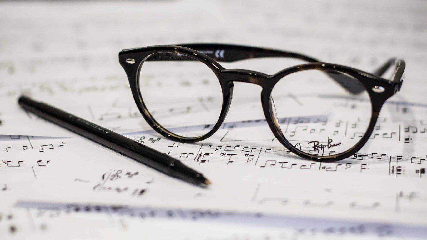 Lunettes posées sur des partitions musicales avec un stylo noir.