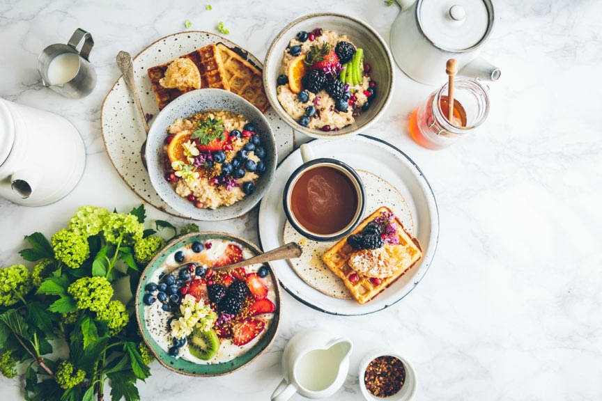 Petit-déjeuner sain avec des bols de fruits frais, du porridge, des gaufres et du café.