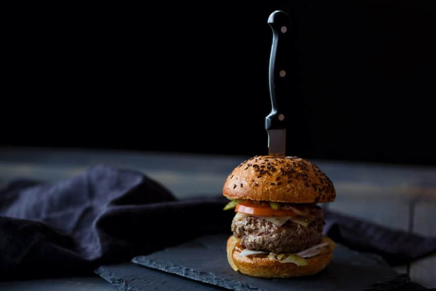 Un burger gourmet avec un couteau planté au centre sur une planche en ardoise.