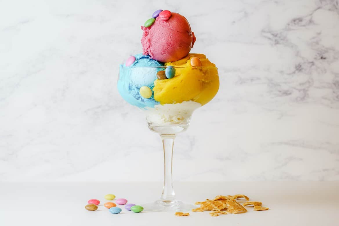 Coupe de glace tricolore avec des bonbons colorés et des éclats de biscuit sur fond marbré.