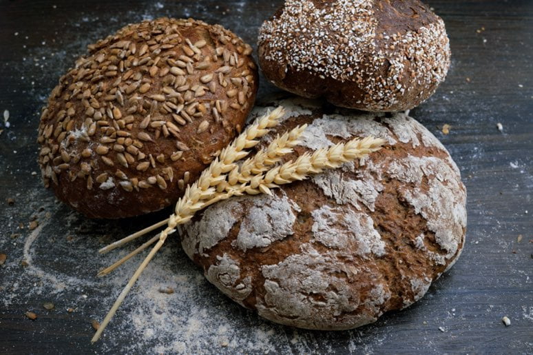 Trois pains rustiques sur une table en bois avec des grains de blé.