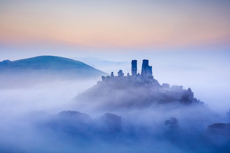 Ruines de château émergeant de la brume au lever du soleil.