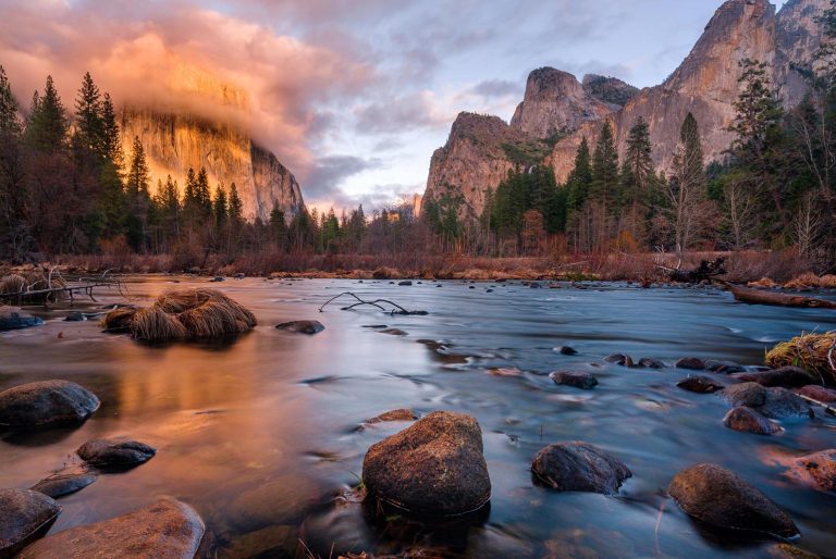 Paysage serein de montagnes au coucher de soleil avec une rivière calme au premier plan.