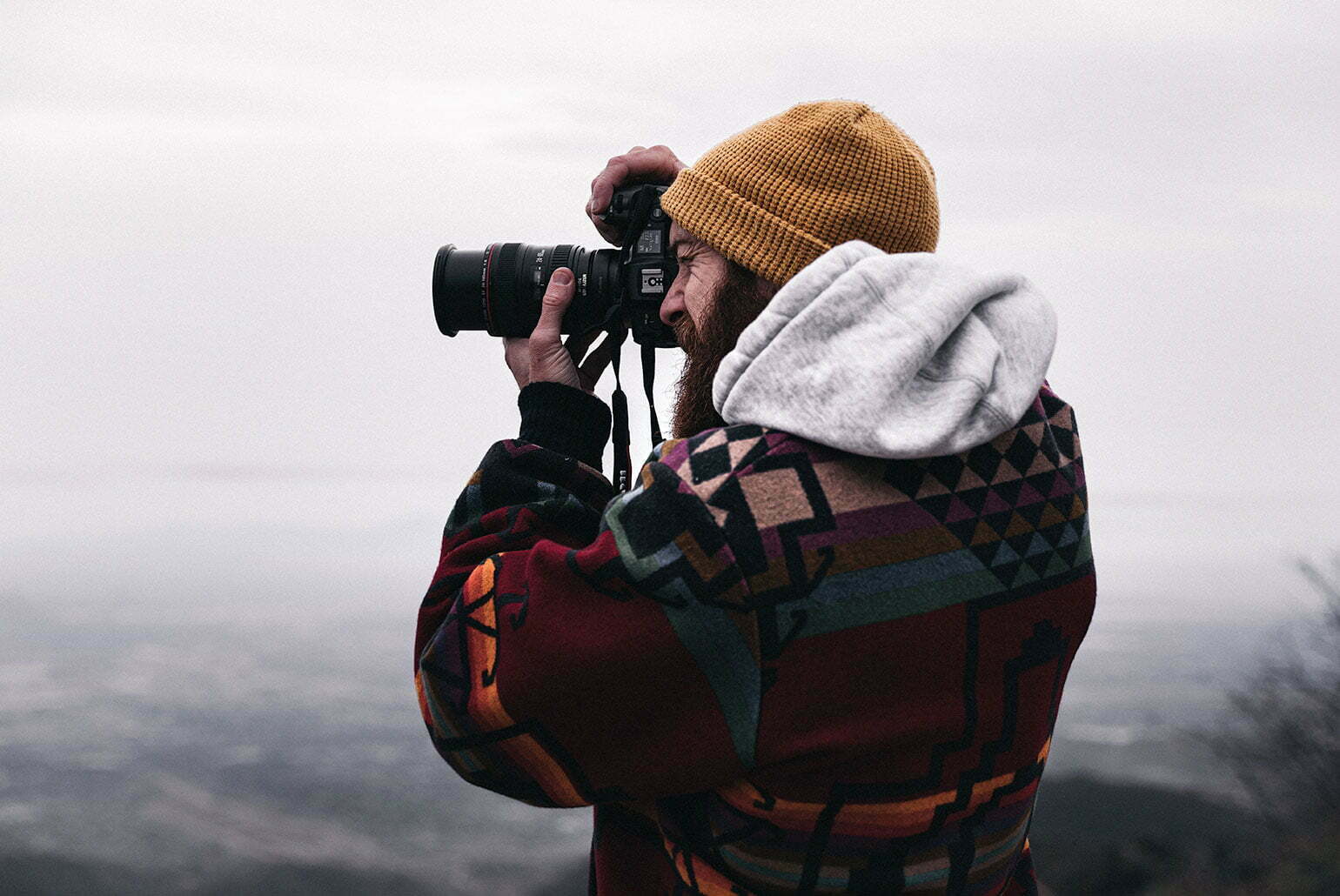 Un photographe barbu avec un bonnet jaune prend une photo en extérieur avec un appareil photo professionnel.