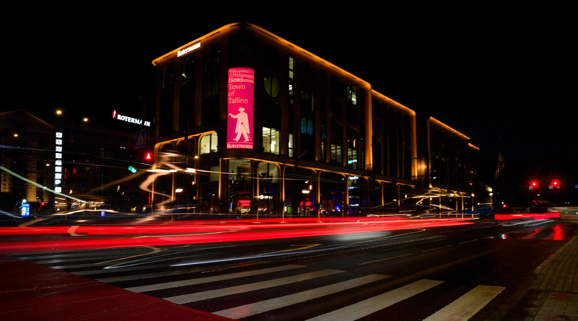 Pose longue de nuit en ville : filés de phares devant un bâtiment illuminé