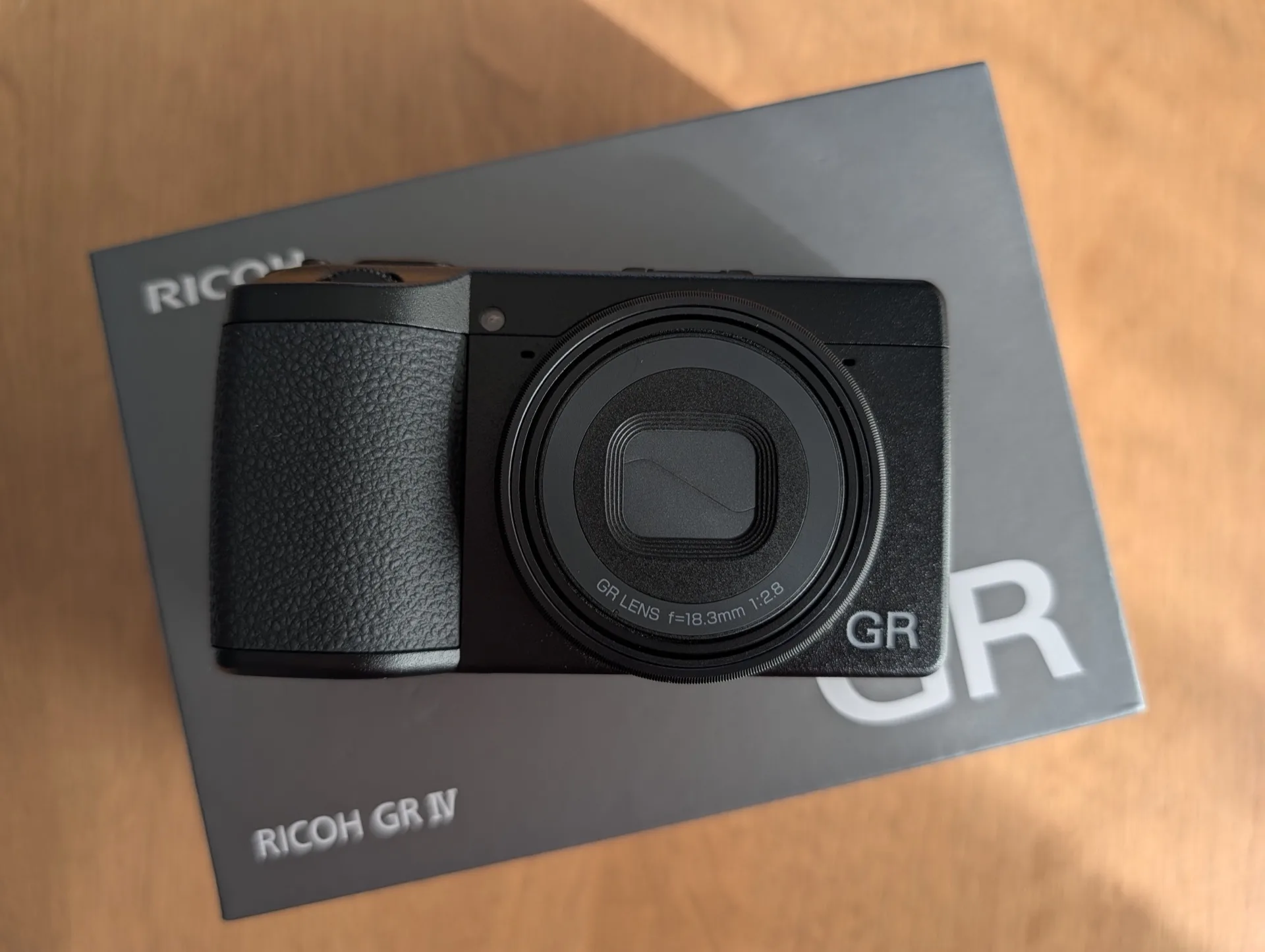 Compact expert Ricoh GR IV posé sur sa boîte, vu de face