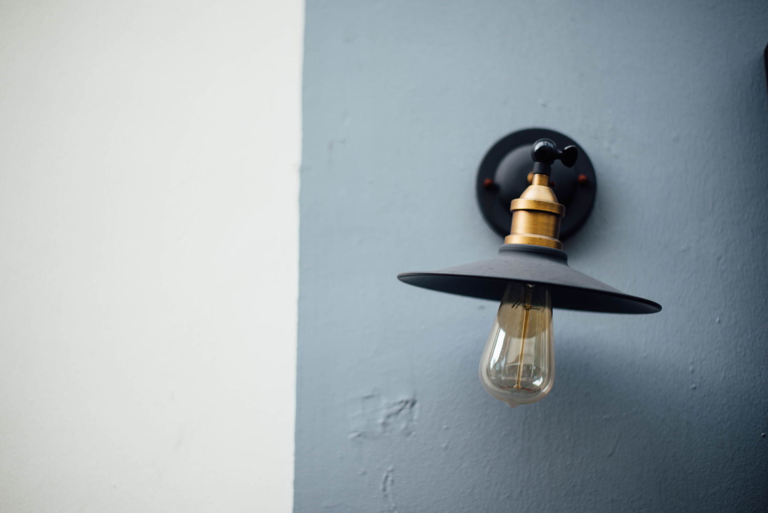 Applique murale noire et dorée avec une ampoule Edison sur un mur bicolore blanc et bleu.