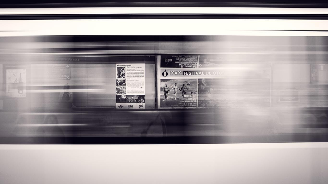 Train en mouvement flou passant devant des affiches sur le quai d'une station de métro.
